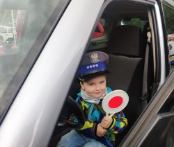 chłopczyk trzyma w dłoni tarczę do zatrzymywania pojazdów i siedzi w radiowozie