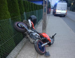 przewrócony motocykl leży na chodniku oparty o ogrodzenie