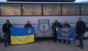 funkcjonariusze trzymający w rękach transparent oraz flagę Ukrainy, w tle autokar IPA
