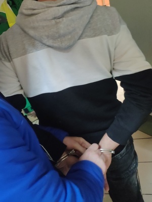 policjant zakłada kajdanki na ręce zatrzymanego