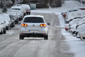 samochód jedzie po jezdni pokrytej śniegiem. Po bokach stoją zaparkowane pojazdy