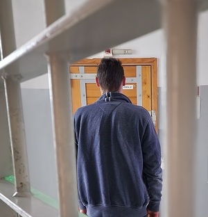 mężczyzna stoi w pomieszczeniu dla osób zatrzymanych za kratami