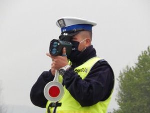 policjant ruchu drogowego ubrany w kamizelkę odblaskową mierzy prędkość ręcznym miernikiem prędkości