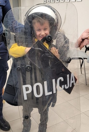 chłopiec w kasku policyjnym w kamizelce i trzyma tarczę z napisem policja