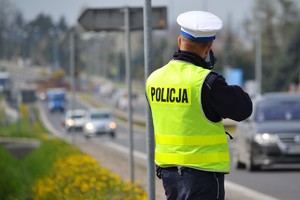 policjant ruchu drogowego w białej czapce i kamizelce odblaskowej mierzy prędkość jadących samochodów