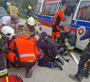 policjant strażacy i ratownicy medyczni udzielają pomocy poszkodowanemu w wypadku w tle karetka pogotowia