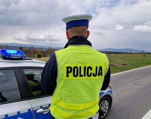 policjant ruchu drogowego w czapce z białym otokiem i kamizelce odblaskowej stoi przy radiowozie