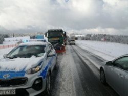 radiowóz policyjny stoi na zaśnieżonej drodze, a za nim piaskarka