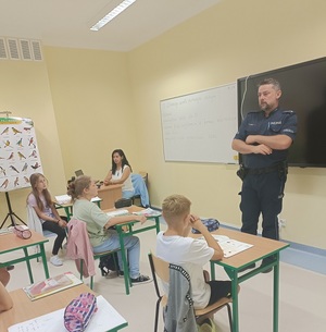 policjant rozmawia z uczniami siedzącymi w klasie