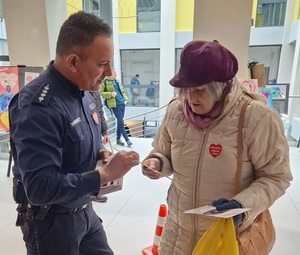 policjant rozmawia z seniorką i wręcza jej ulotkę