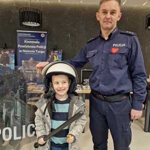 policjant z chłopcem ubranym w kask na głowie i pałką w ręku