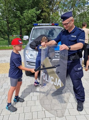 policjant trzyma tarczę a chłopiec pałką uderza w tarczę