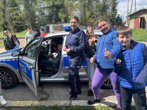Dzieci i policjantka stojąca obok radiowozu