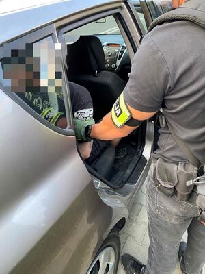 Policjant nieumundurowany który trzyma zatrzymanego siedzącego w radiowozie