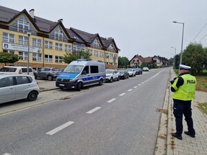 Policjant stojący pod szkołą a obok radiowóz
