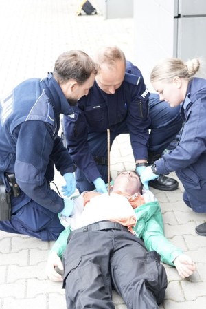 Trzech policjantów i poszkodowany z wsytajacym pretem z klatki piersiowej
