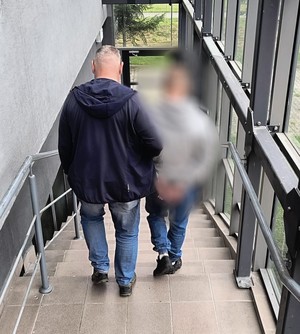 Nieumundurowany policjant prowadzi zatrzymanego po schodach