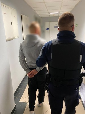Policjant w mundurze prowadzi zatrzymanego w kajdankach