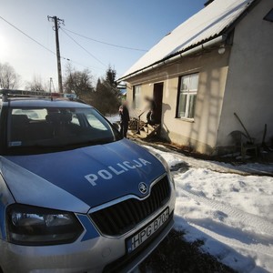 policyjny radiowóz przed domem w tle policjant i męzczyzna wychodzący do niego