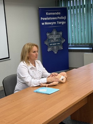 kobieta siedzaca przy stole na stole lezy fantom noworodka