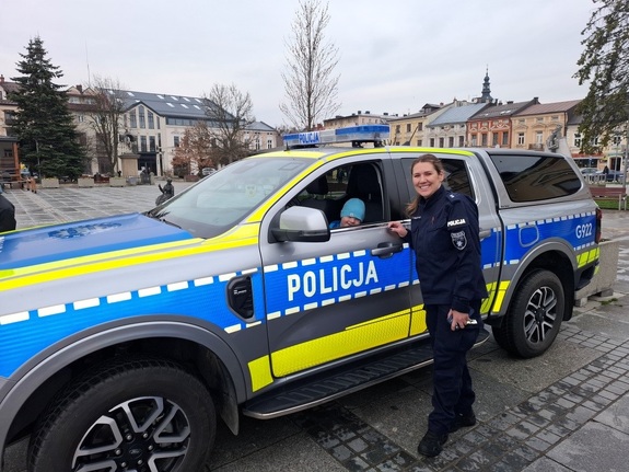 Policjantka obok radiowozu za jego kierownica siedzi dziecko