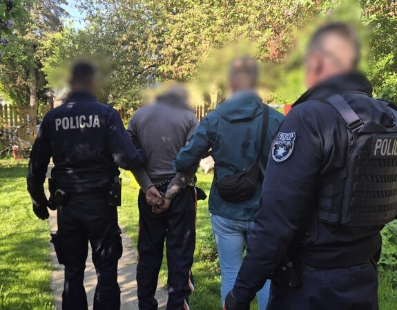 dwóch policjantów w mundurach oraz zatrzymany mężczyzna w kajdankach