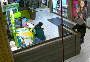 nieletni chłopak próbuje okraść automat do gier obok kuca jego kolega, po prawej stronie chłopak w czarnej kurtce stoi na czatach
