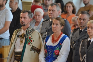 kobieta i mężczyzna w stroju góralskim stoją w kościele w tle policjanci